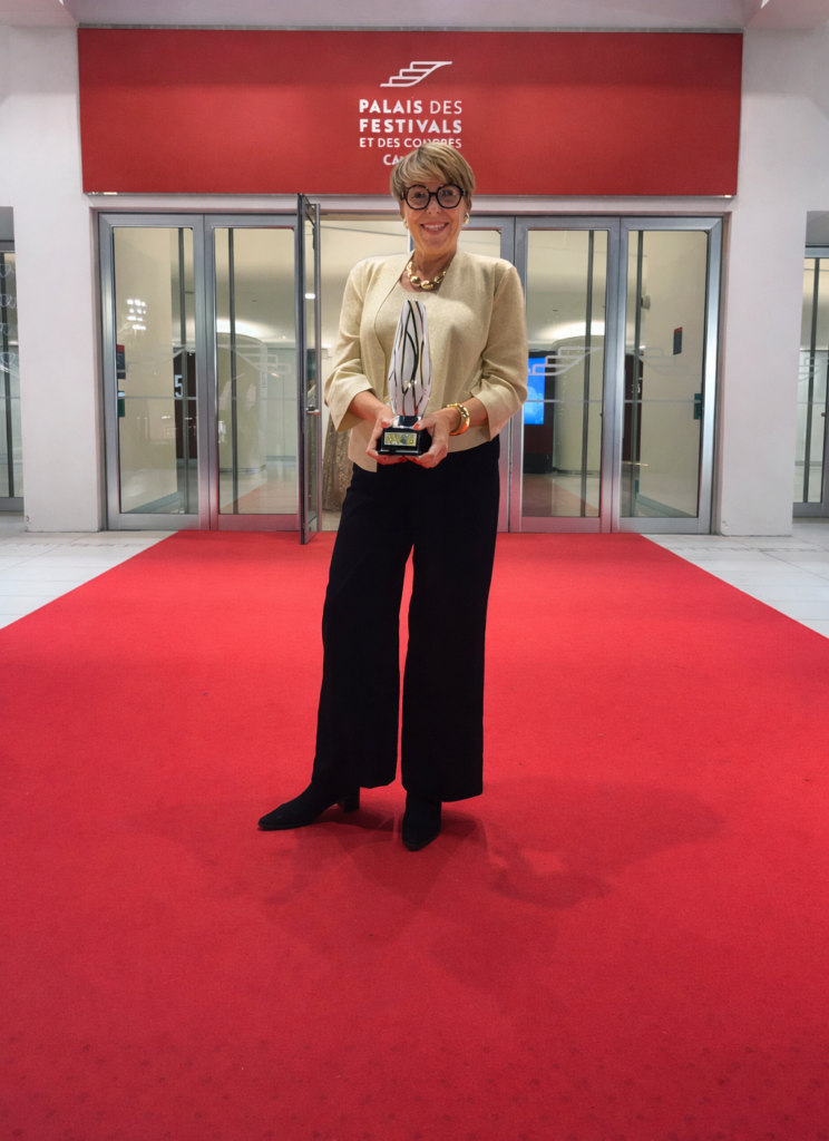 Sandrine Mercy en haut des marches du Palais des Festivals de Cannes, tenant le Prix Lys d’Or